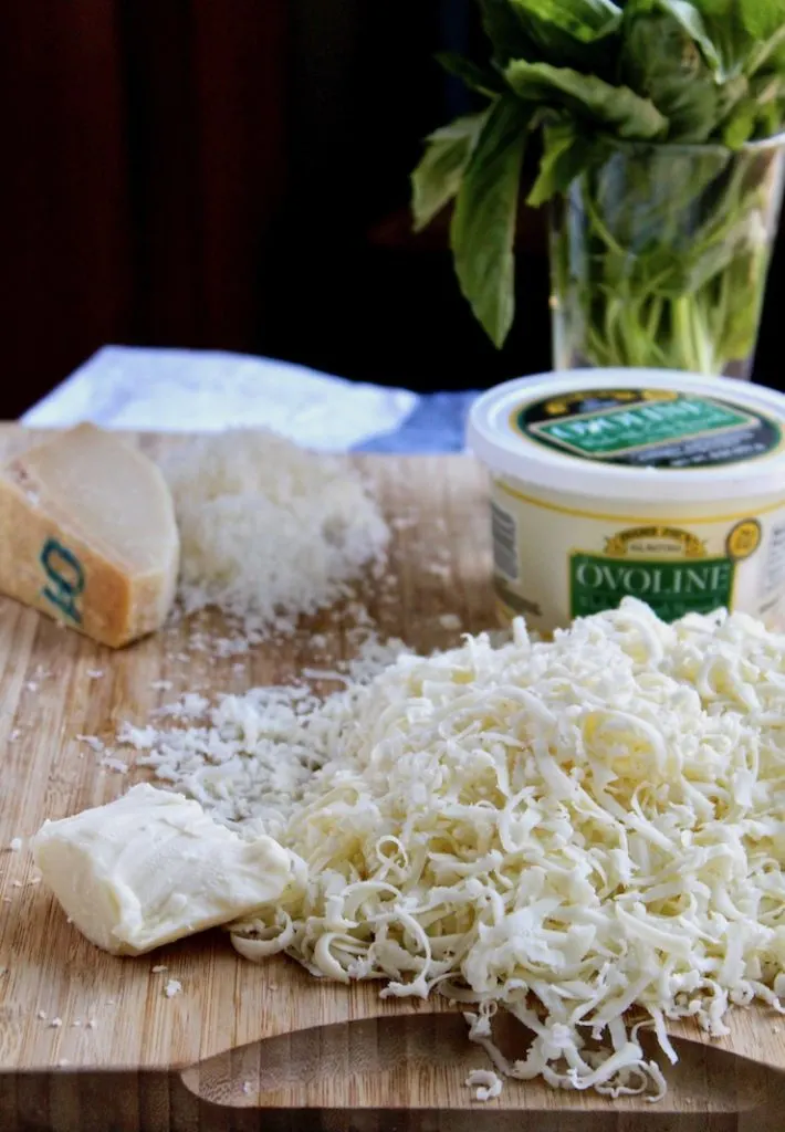 Shredded mozzarella, parmesan and fresh mozzarella on cutting board