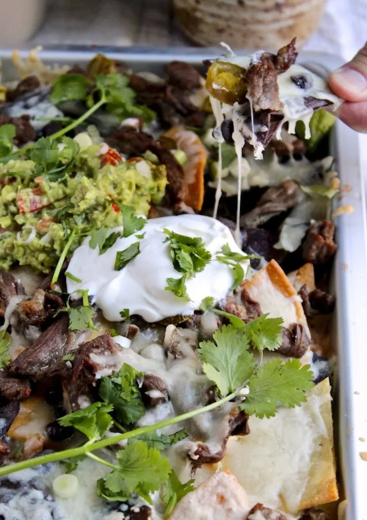 Hand scooping up a loaded tortilla chip out of sheet pan.