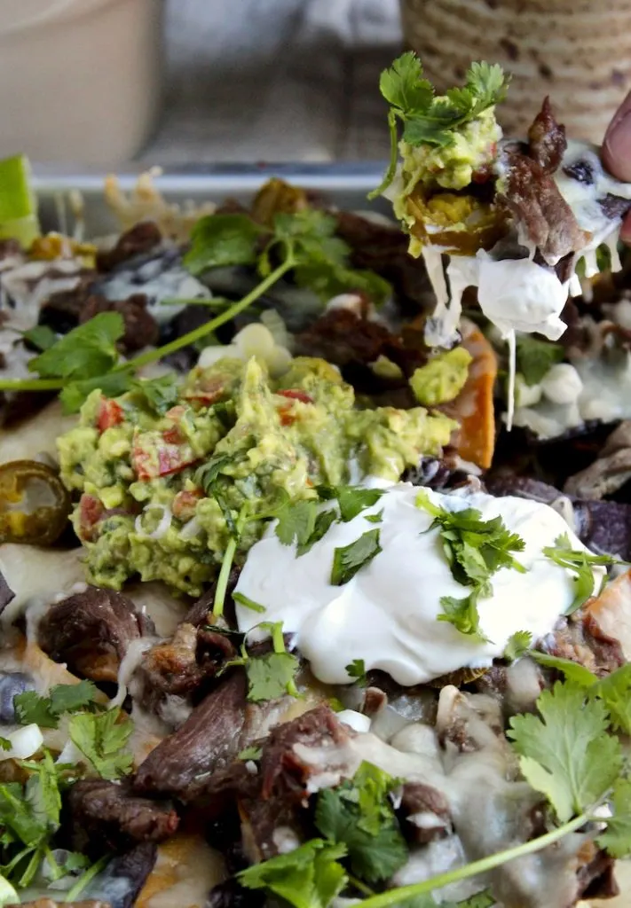 Loaded Steak Nachos, hand scooping up some nachos.