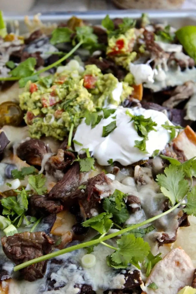 Close up of steak nachos and toppings in sheet pan.