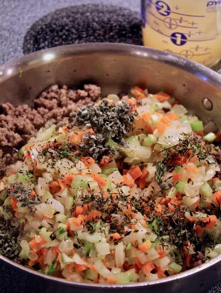 Sausage, vegetables and fresh herbs cooking in skillet.