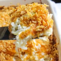 Cheesy potatoes close up on spatula above casserole dish.