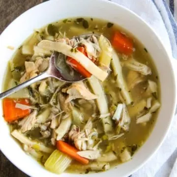 Turkey noodle soup with spoon in white bowl.