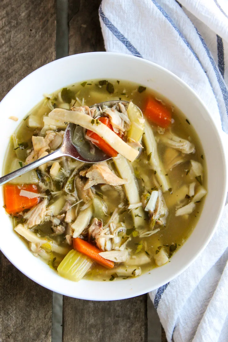 Turkey noodle soup with spoon in white bowl.