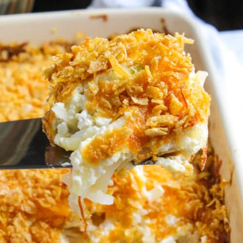 Cheesy potatoes on spatula above casserole.