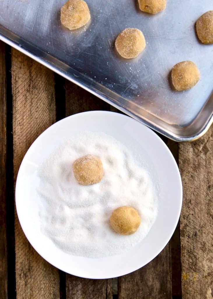 Rolling balls in sugar, placing on baking sheet.