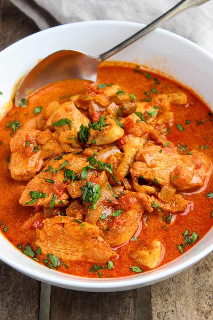 Chicken paprikash in white serving bowl with spoon.