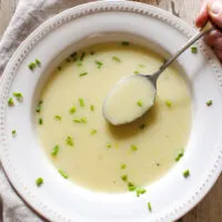 Spoonful of potato leek soup over bowl garnished with chives.