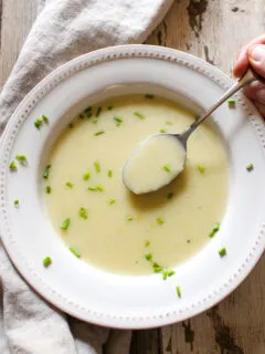 Spoonful of potato leek soup over bowl garnished with chives.