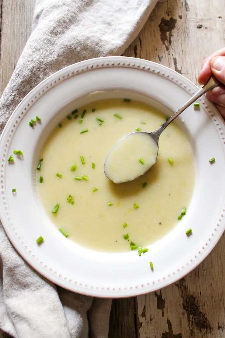 Spoonful of potato leek soup over bowl garnished with chives.