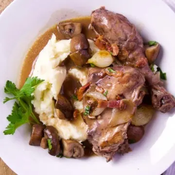 Coq au vin in serving dish with mashed potatoes.