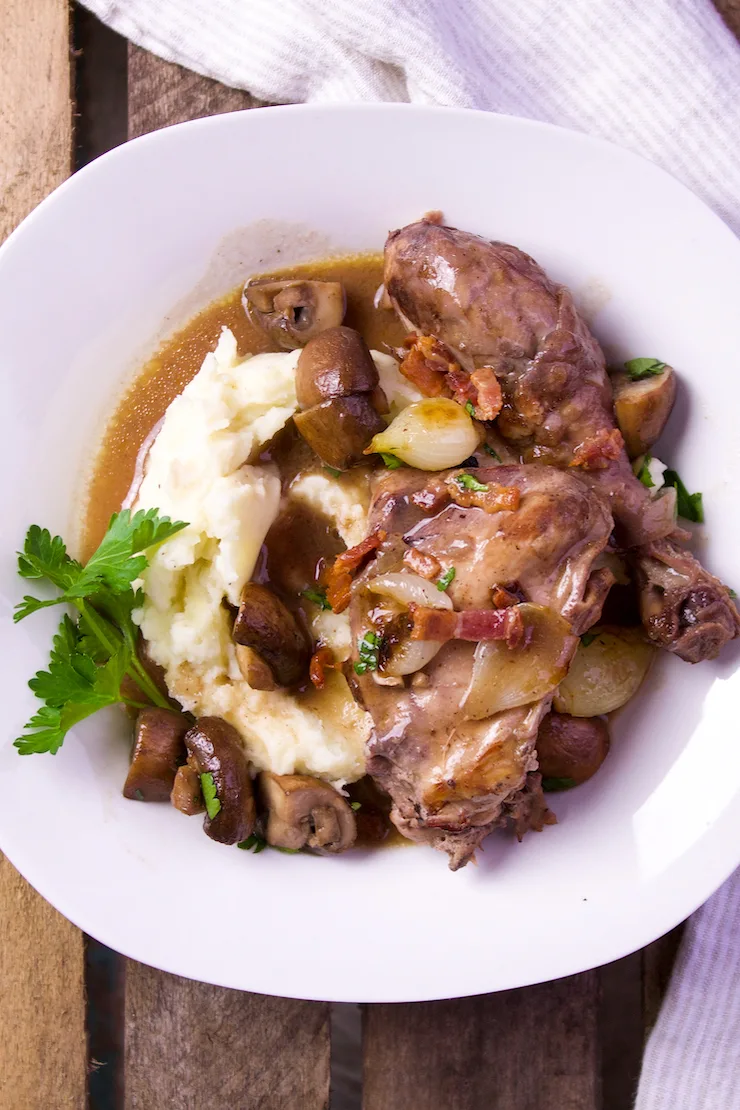 Coq au vin in serving dish with mashed potatoes.