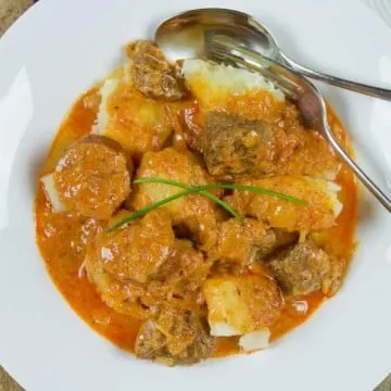 Pork and sauerkraut goulash in serving bowl with boiled potatoes.