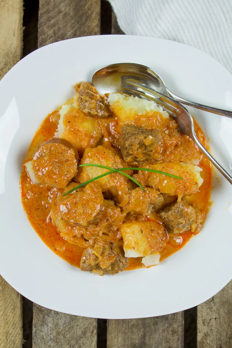 Pork and sauerkraut goulash in serving bowl with boiled potatoes.