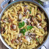 Pasta with bacon, onion and mushrooms in skillet with parmesan cheese.