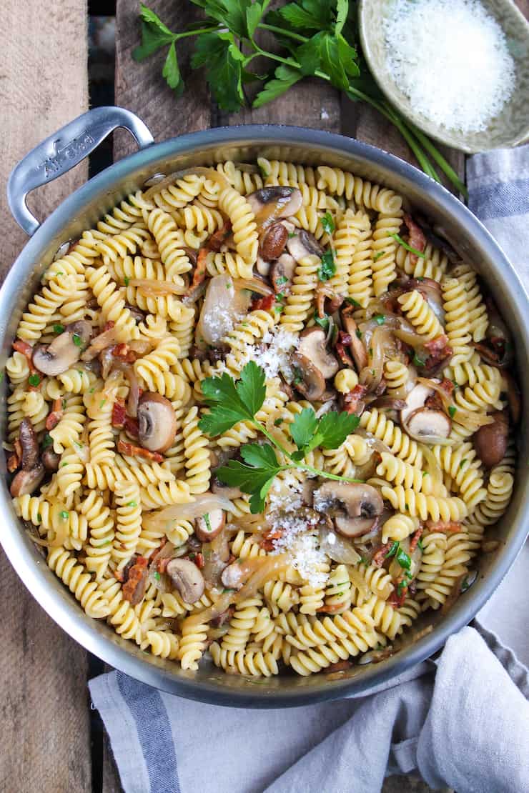 Pasta with bacon, onion and mushrooms in skillet with parmesan cheese.