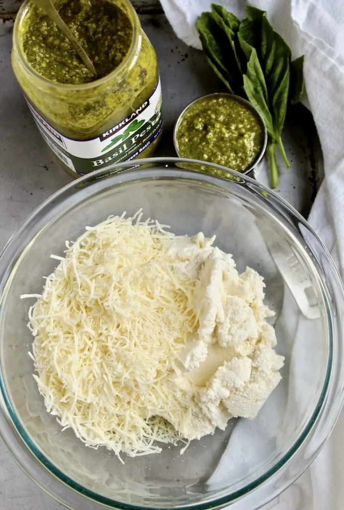 Cheeses in bowl and jar of pesto ingredients.
