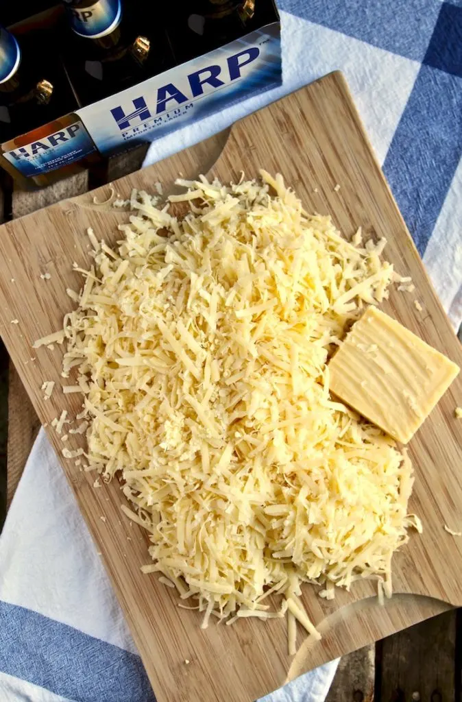 Irish Beer Cheese Soup, shredded cheese on cutting board with beer in background.