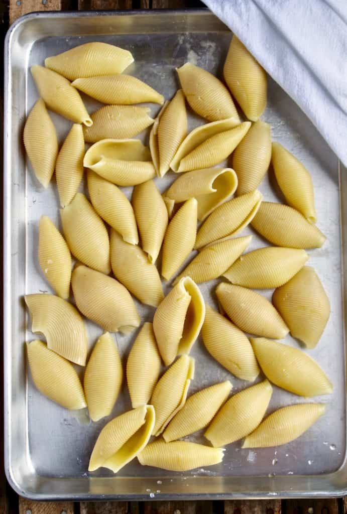Cooked pasta shells cooling on sheet pan.