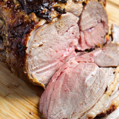 Mustard and herb roasted lamb on cutting board sliced.