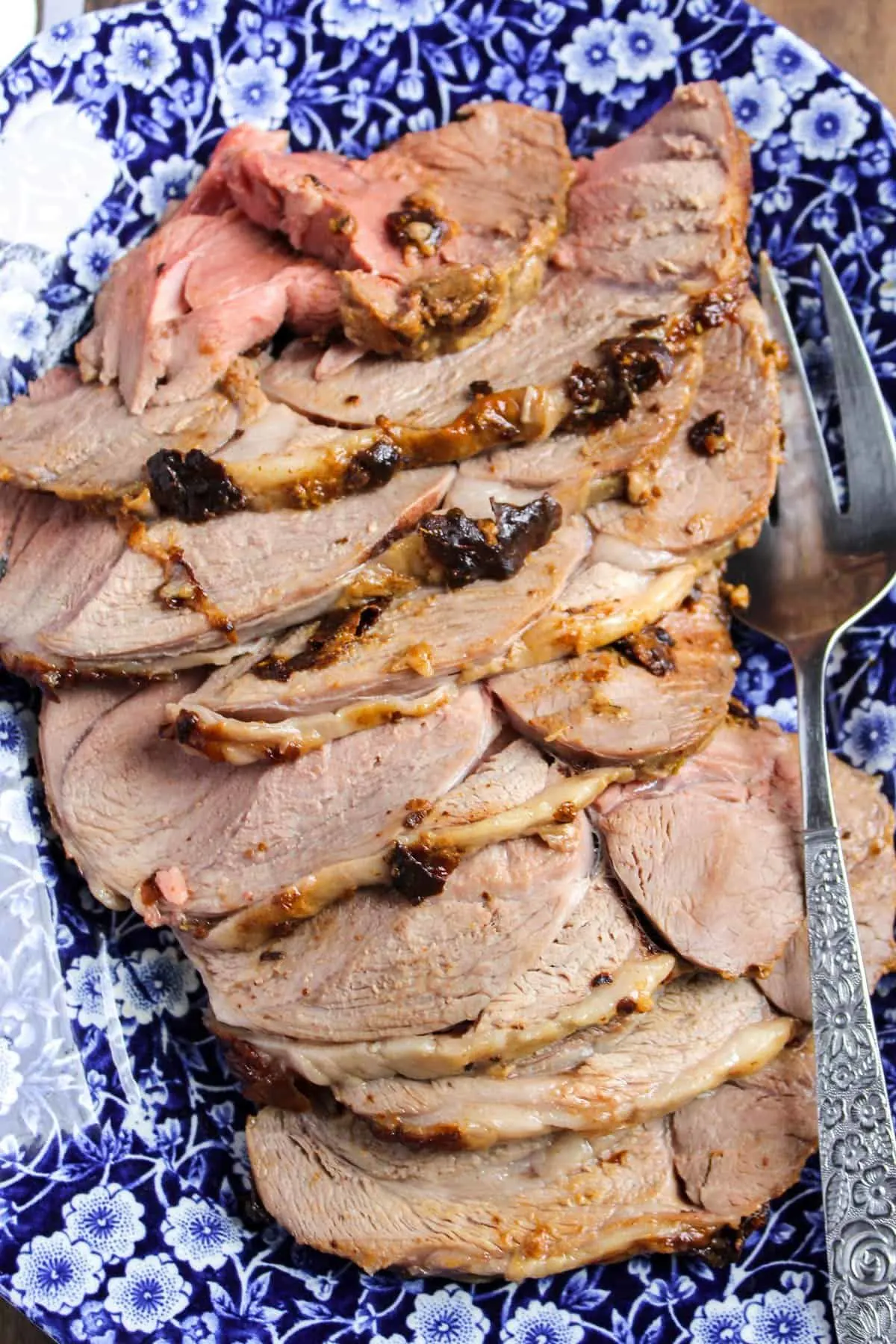 Slices of mustard and herb roasted boneless leg of lamb on blue and white serving platter.