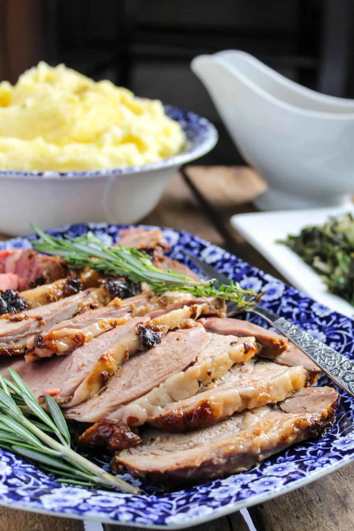 Lamb slices on serving platter with gravy and side dishes in background.