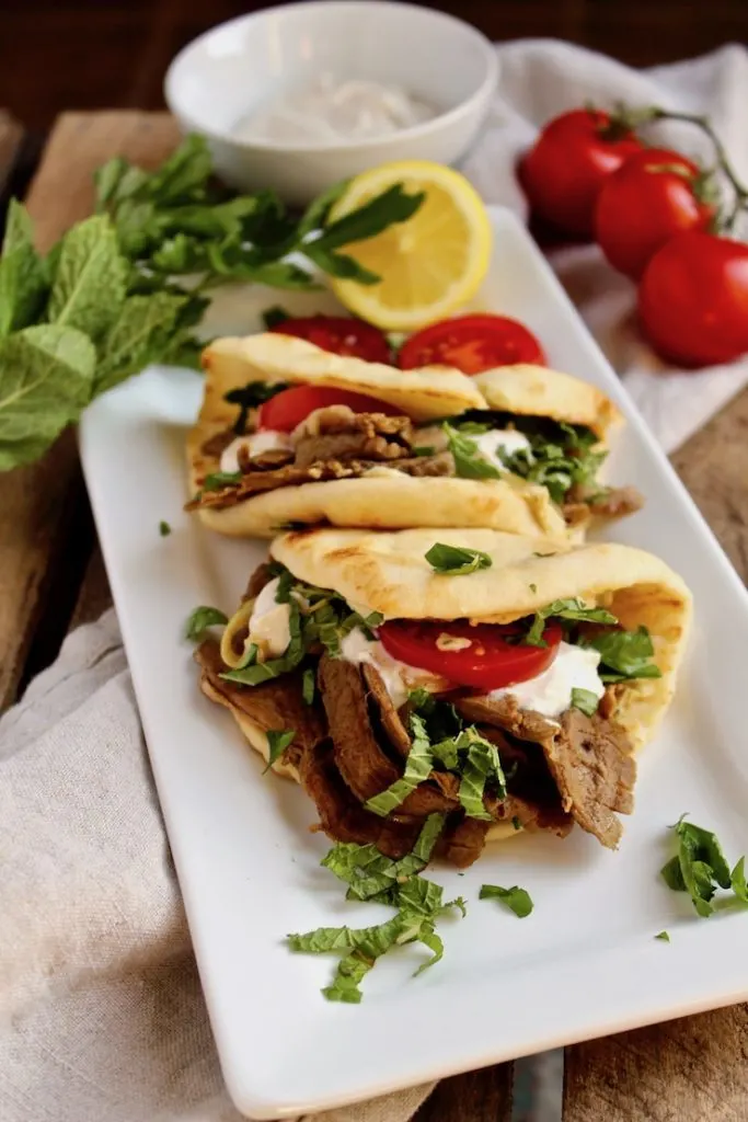 Leftover Lamb Flatbreads, on serving platter, yogurt sauce, tomatoes and herbs in background.