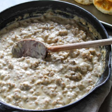 Sausage gravy in skillet with wooden spoon.