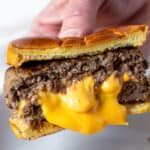 Hand holding Juicy Lucy burger with melted cheese center.