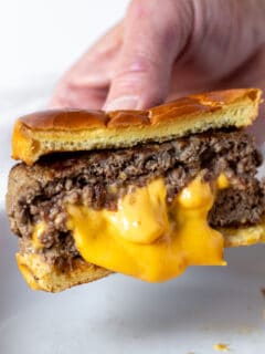 Hand holding Juicy Lucy burger with melted cheese center.