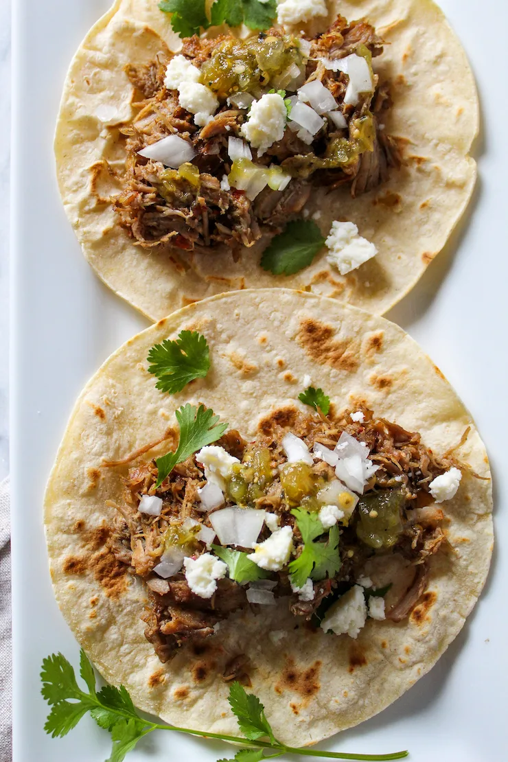 Tacos de carnitas with toppings on tortilla.