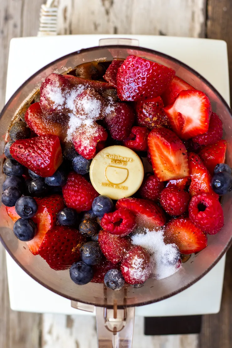 Berries and ingredients in bowl of food processor.