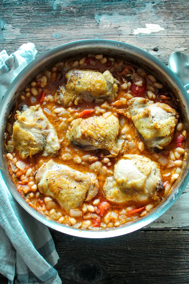 Overhead of chicken and white beans in skillet.