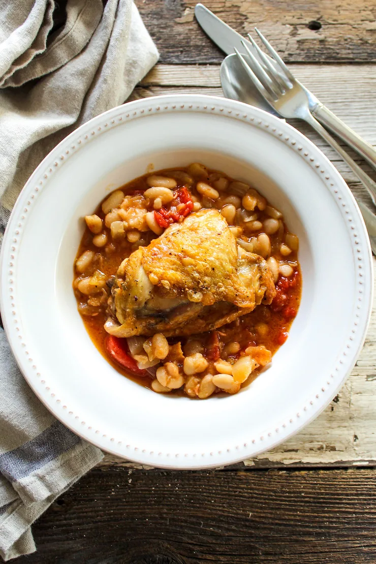 Plated chicken thigh over white beans.