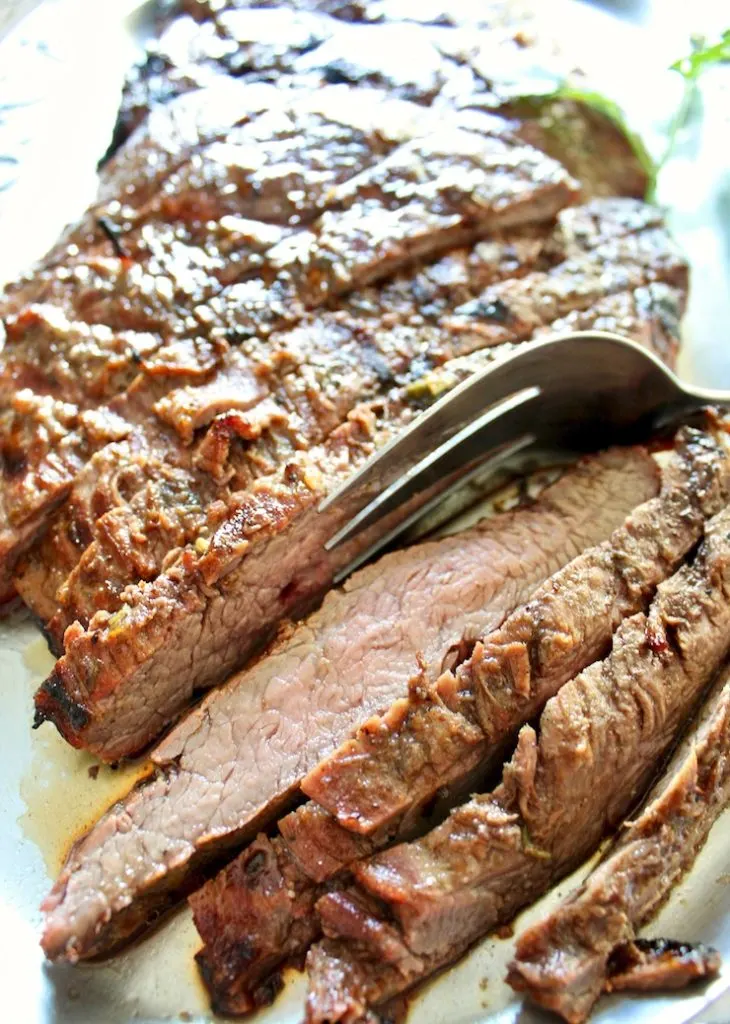 Close up of sliced flank steak on platter with fork.