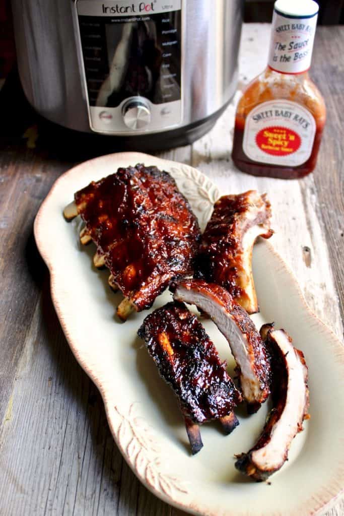 Instant Pot Barbecue Ribs on serving platter with Instant Pot and BBQ sauce in background