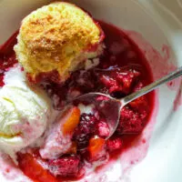 Closeup of blackberry peach cobbler with spoon and melting ice cream.