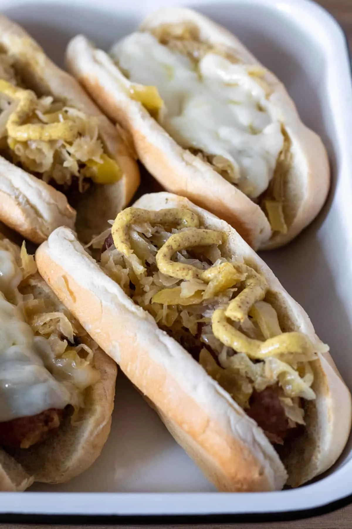 Closup of brats on buns with mustard and melted cheese.