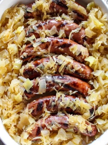 Brats and sauerkraut in white serving dish.