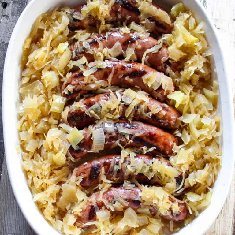 Brats and sauerkraut in white serving dish.
