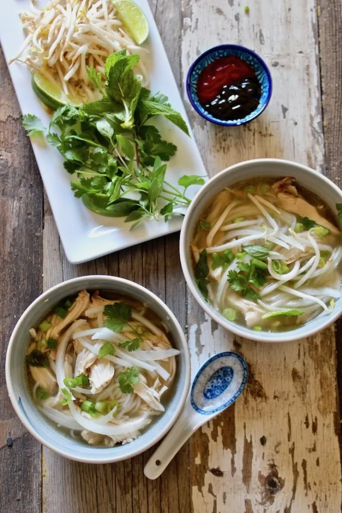 Overhead of two bowls of pho and condiments