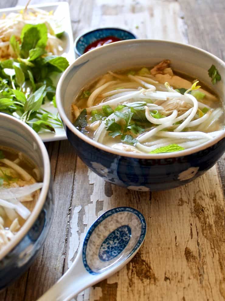 Instant Pot Pho Ga, in bowl surrounded by condiments and spoon