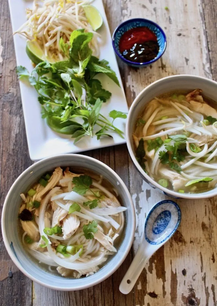 Two bowls of Instant Pot pho ga with condiments and spoon