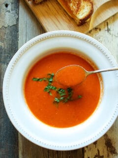 Spoonful of tomato bisque hovering over bowl of soup.