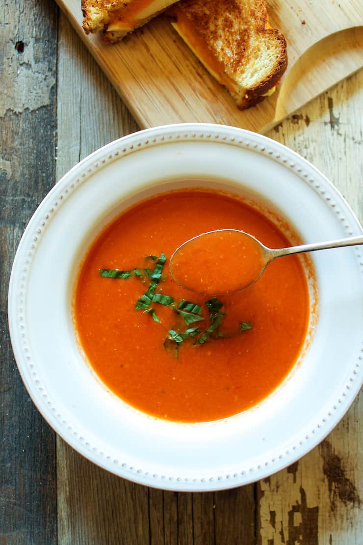 Spoonful of tomato bisque hovering over bowl of soup.