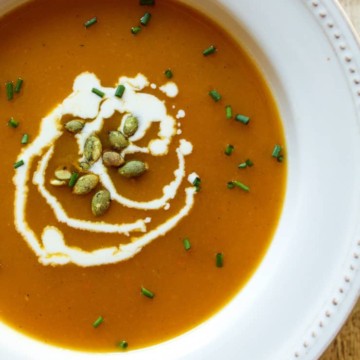 Close up of squash soup in bowl garnished with cream and pumpkin seeds.