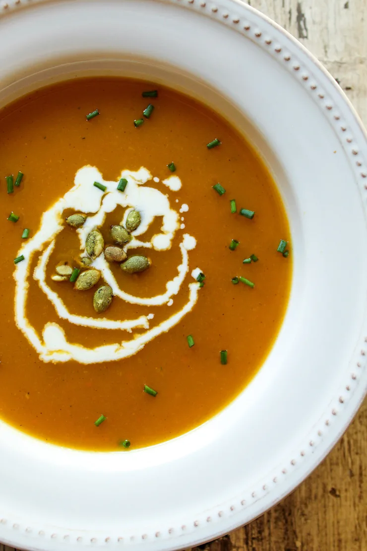 Close up of squash soup in bowl garnished with cream and pumpkin seeds.