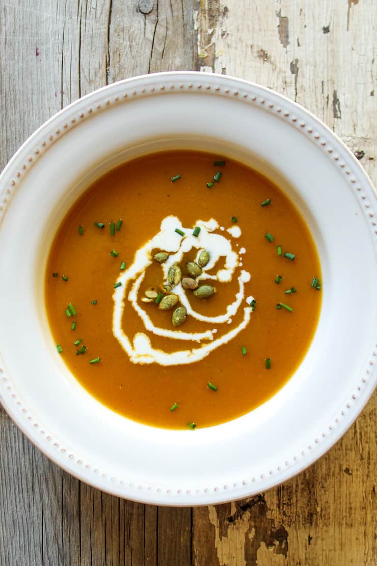 Squash soup in bowl garnished with pumpkin seeds and cream.