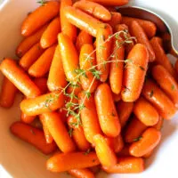 Glazed carrots in white serving bowl with fresh thyme.