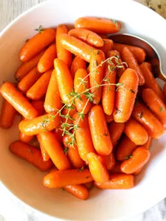 Glazed carrots in white serving bowl with fresh thyme.
